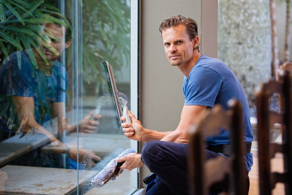 man-in-blue-crew-neck-shirt-634007 A man in a blue t-shirt cleaning large glass pane with a squeegee indoors.